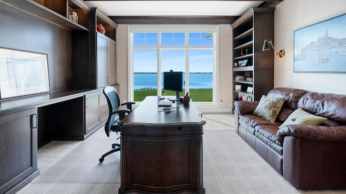 Classy home office with dark oak desk and couch with views of a lake